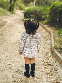 Niña de espaldas con Jesusito manga larga de cuadros multicolor con fondo blanco Colección Almendro | MICŪ baby
