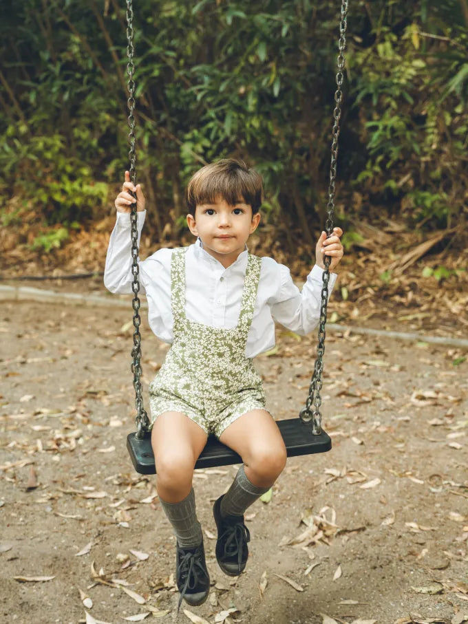 Niño sentado con pantalón de tirantes verde con flores blancas Colección Helecho | MICŪ baby
